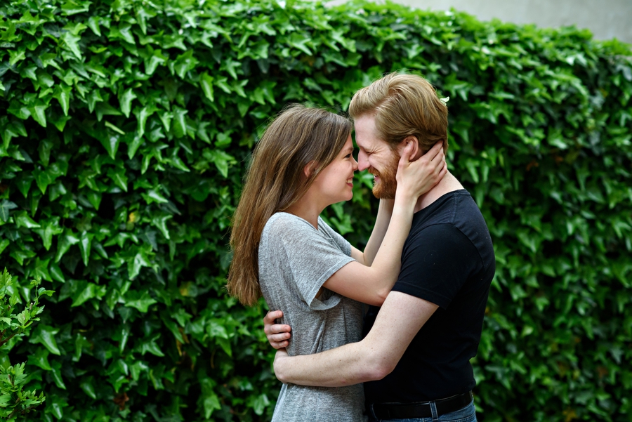 A bride to be holds her fiance's face in front of a wall of ivy in their philadelphia engagement session.